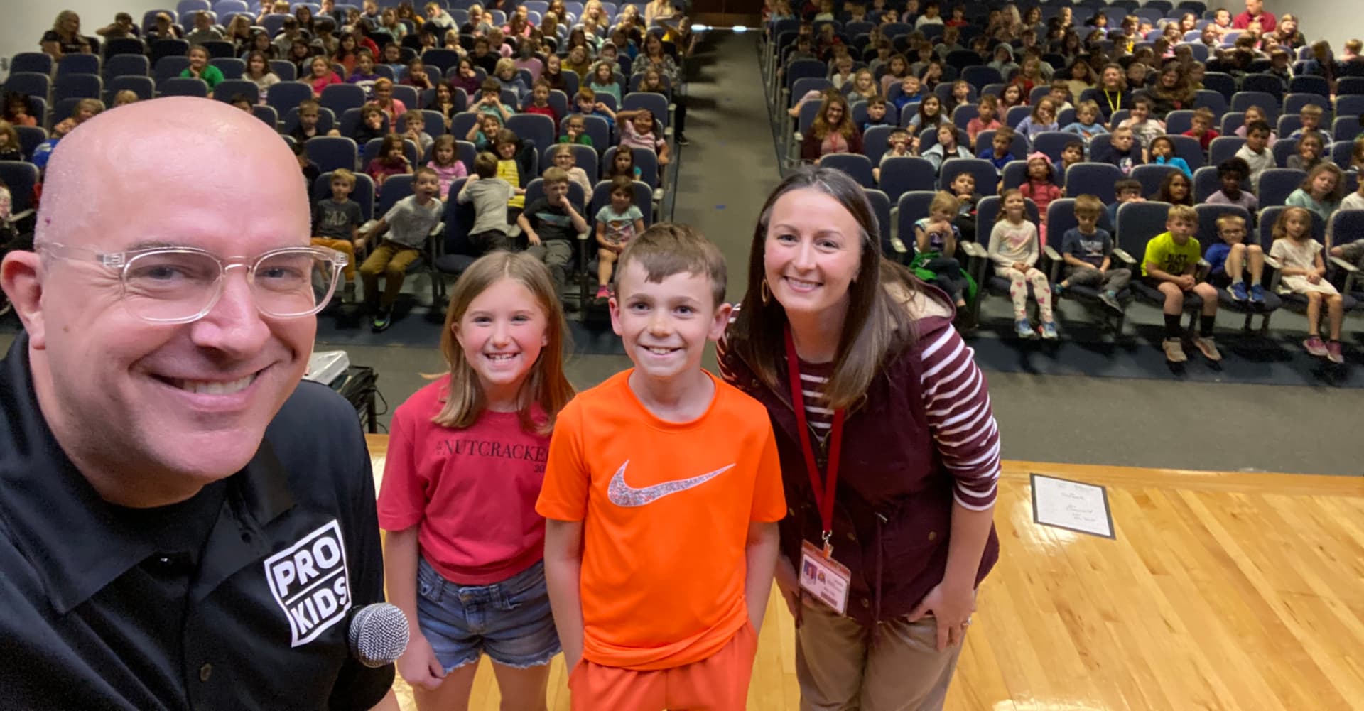 A Husmann teacher and student helpers on stage during a daytime assembly