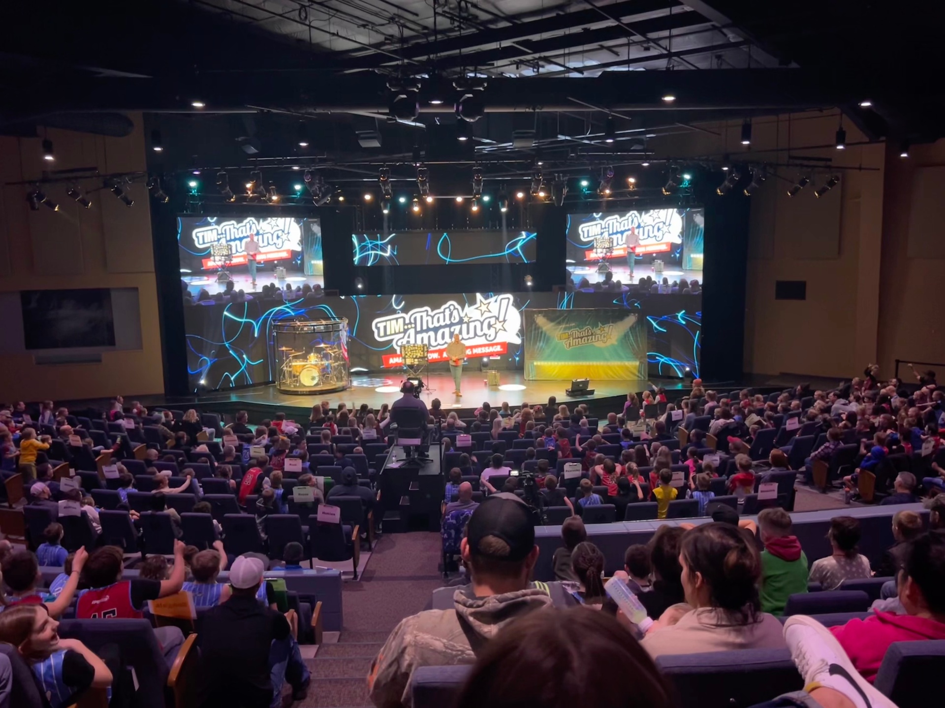 Tim performing on a large concert-style stage with big video screens and stage lighting in front of a full audience