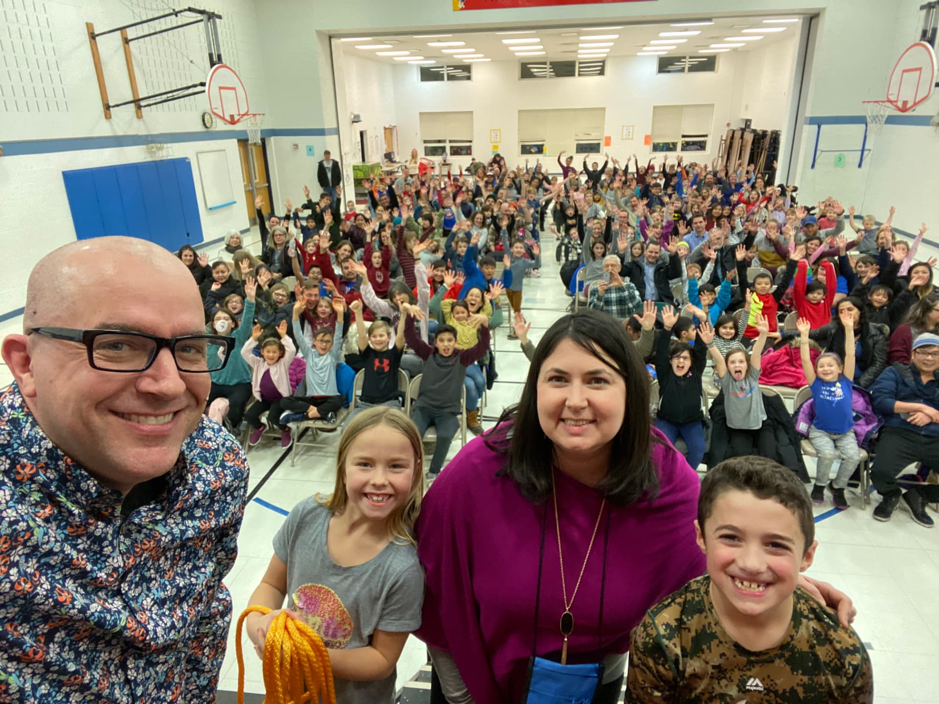Tim Hannig with a teacher and students in front of a large waving crowd at Hawthorne Family Night