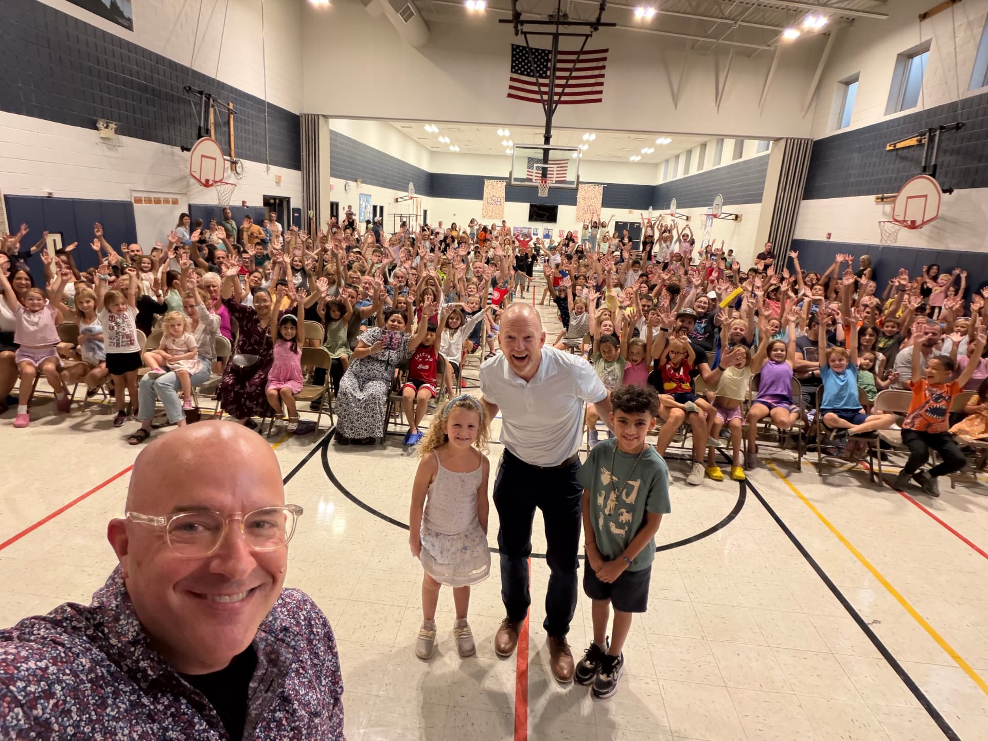 A packed Family Night crowd at Madison Elementary with hands in the air